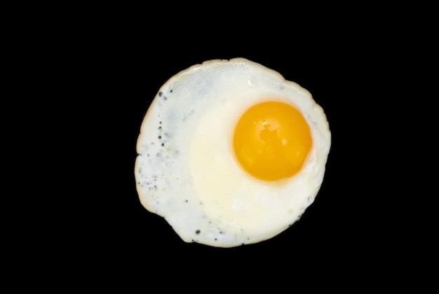 Top view of a sunny side up fried egg isolated on a black background in closeup