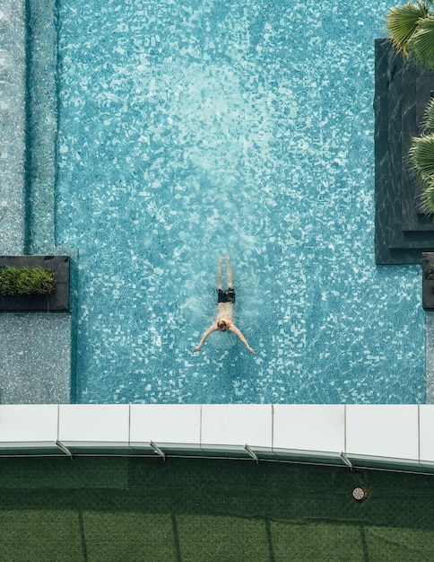 Top view of swimming pool with floating bar and a man swimming\
in summer.