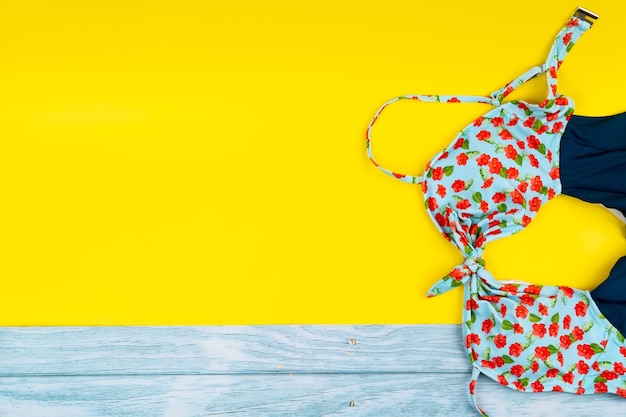 Top view of the swimsuit lying on a blue wooden and yellow background.Summer vacation concept