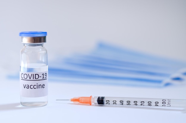 Вид сверху на шприц с медицинскими масками и стеклянными бутылками с вакциной для вакцинации. COVID-19