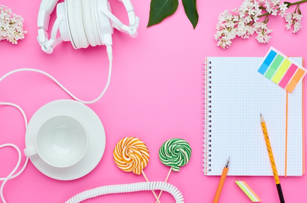 Top view of the table of a teenage child, composition of pencil for laptop eraser flower glass with drink earphone Lollipop on pink background