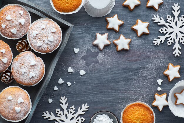 Top view of the table with sugar sprinkled muffins, fondant icing and Christmas star cookies on dark wood