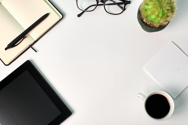 Vista dall'alto di un tablet, una tazza di caffè, una pianta, un taccuino e bicchieri su sfondo bianco. copia spazio