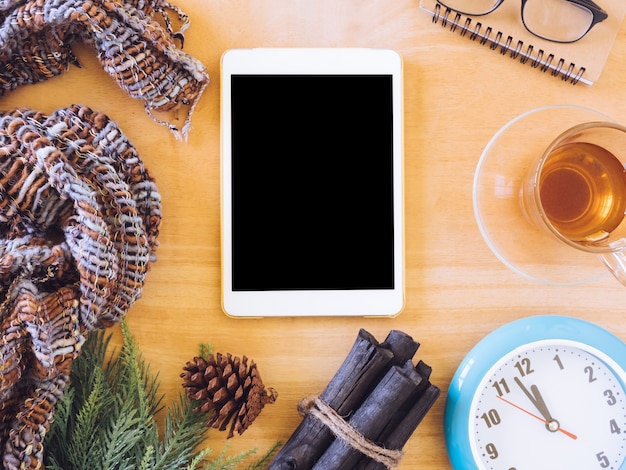 Top view of tablet with tea cup,clock, scarf and christmas decoration on wooden table.