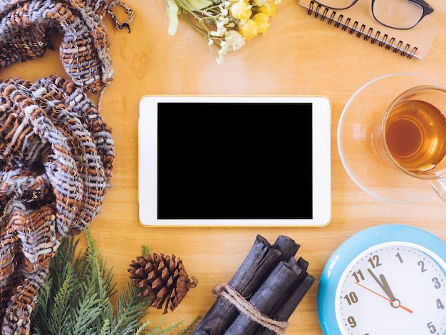 Top view of tablet with tea cup,clock, scarf and christmas decoration on wooden table.