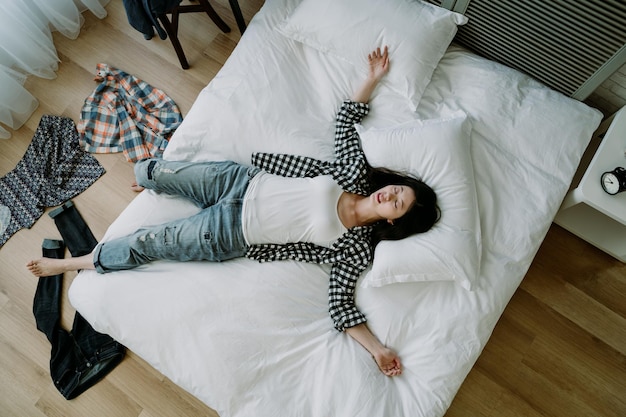 Top view of taiwanese woman lying in a sprawl on bed with her
clothes scattered on floor. asian young girl hanging out with
friend until dawn goes to bed straight without taking bath.