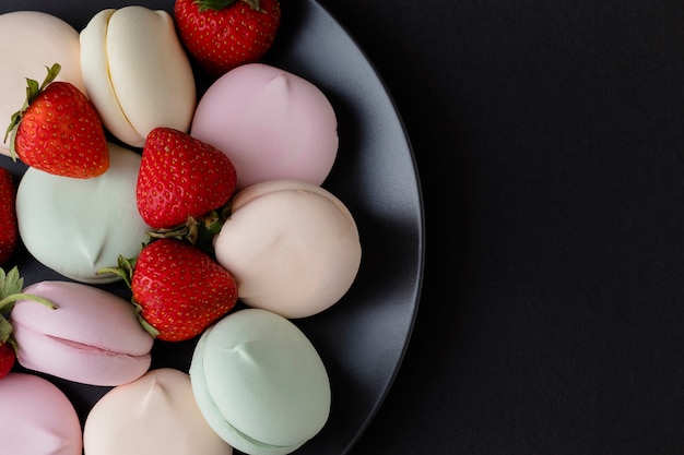 Top view of tasty colorful marshmallows with strawberry on black plate