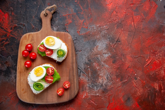 top view tasty egg sandwiches with red tomatoes on cutting board dark red background lunch toast snack burger sandwich food bread meal free space