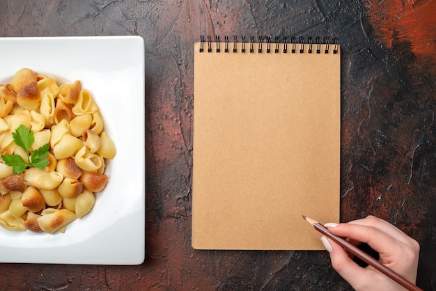 top view tasty pasta on plate pencil in female hand notebook on wooden table