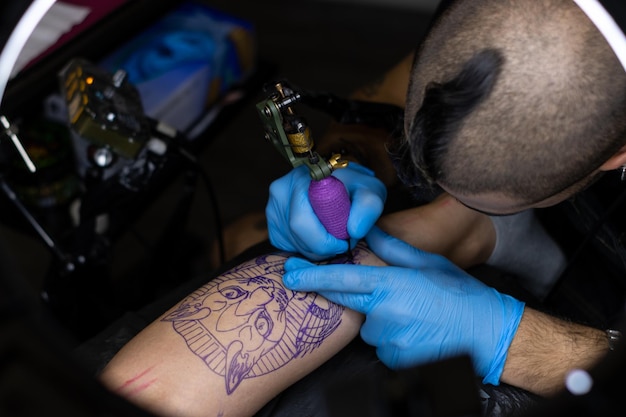 Top view of Tattooist tattooing a young woman's leg stretched out on a stretcher in a tattoo studio