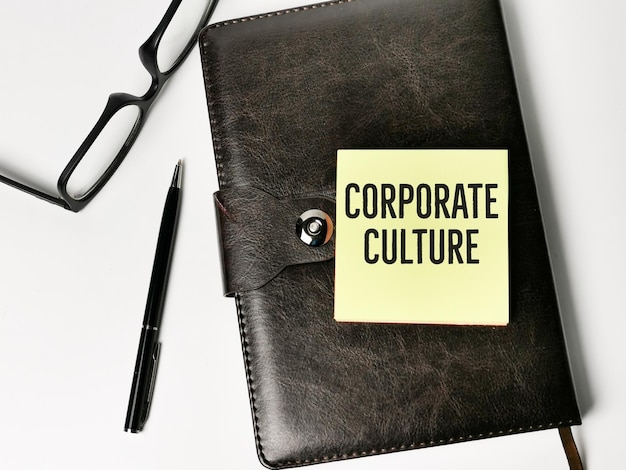 펜과 일기장이 있는 스티커 메모에 쓰여진 상위 뷰 텍스트 CORPORATE CULTURE.