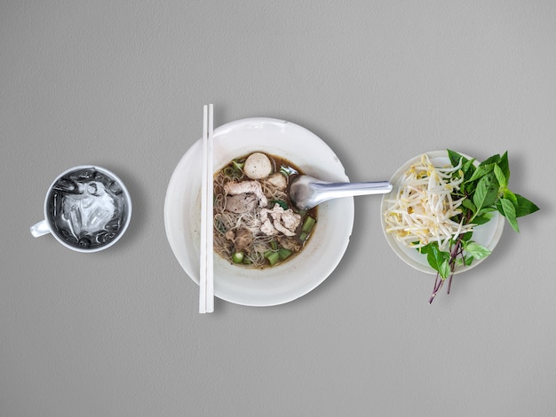 Top view of Thai rice noodles thicken soup with vegetables set and ice water cup.