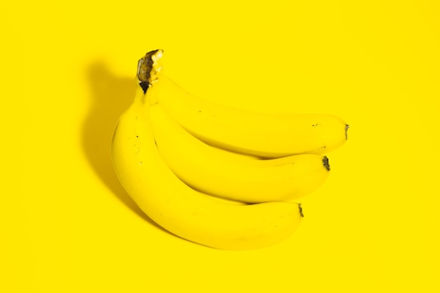 Top view of three bananas on surface of yellow color.