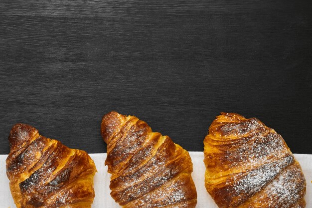 Top view of three croissants on a black background with copy space. Delivery of products