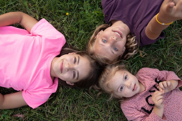 Top view of three girls laughing while lying on the grass outside. Carefree happy childhood concept