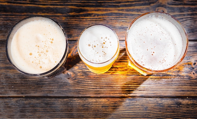 Top view of three glasses with light, unfiltered and dark beer on wooden desk. Food and beverages concept