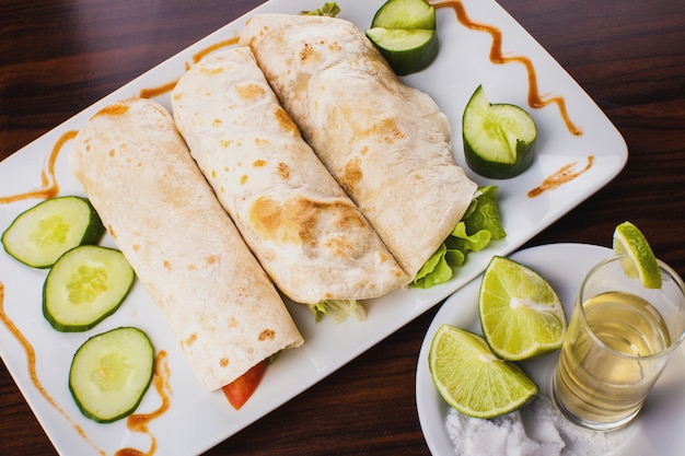 Top view of three mexican tortillas wraps with tequila, lemon and salt on wooden table
