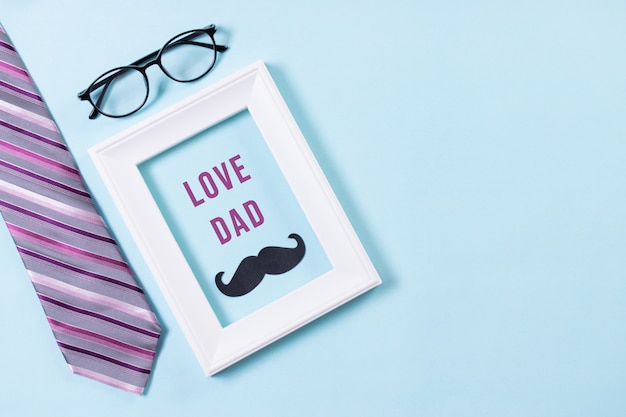 Photo top view of tie, glasses, mustache with love dad text on blue pastel background