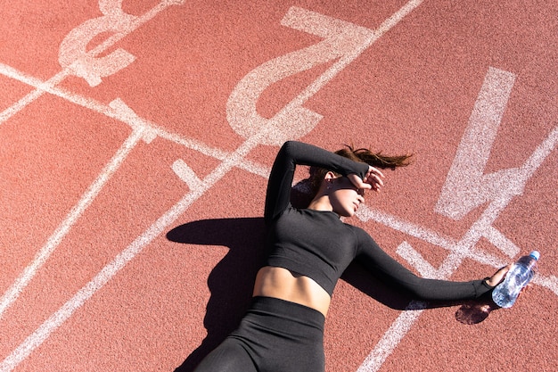 Foto vista dall'alto della donna in forma stanca in abiti sportivi che riposa dopo l'allenamento o in esecuzione su uno stadio di gomma del tapis roulant