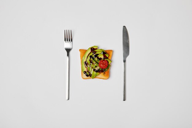 アボカドとチェリー トマトのフォークとナイフ グレーに分離されたトーストの平面図