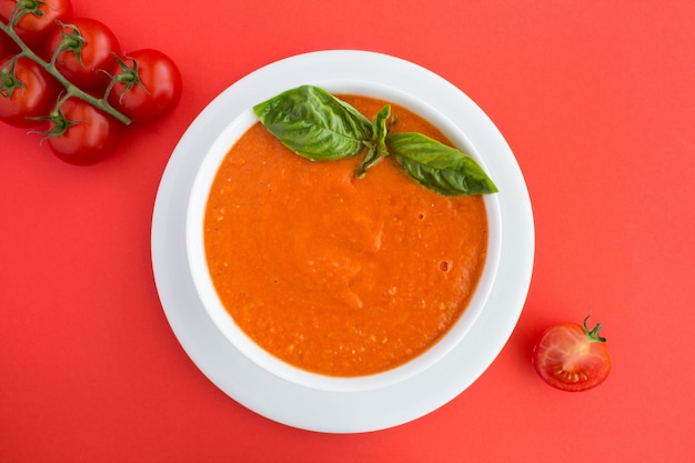 Top view of tomato soup in the white  bowl on the red surface