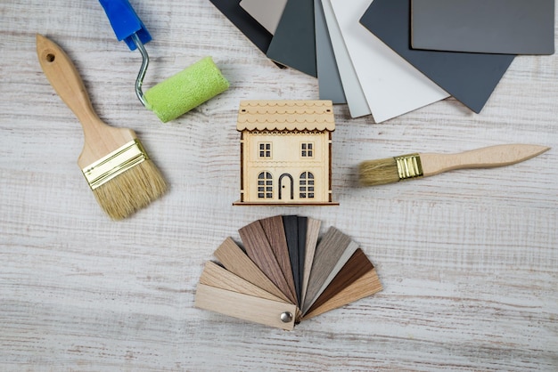 Top view of a toy wooden house with a color palette and brushes\
for apartment renovation or house renovation