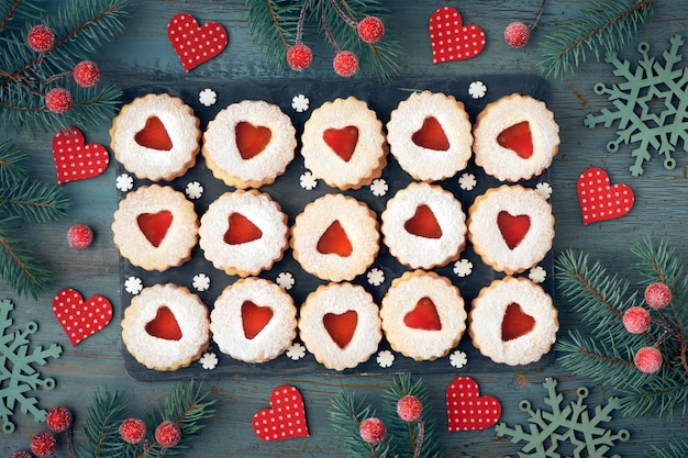 Top view of traditional Christmas Linzer cookies with red jam on rustic wood decorated with berries