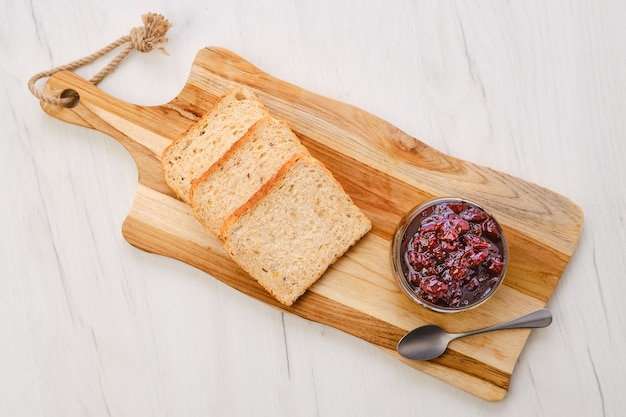 Top view of transparent pot with cherry jam and toast bread