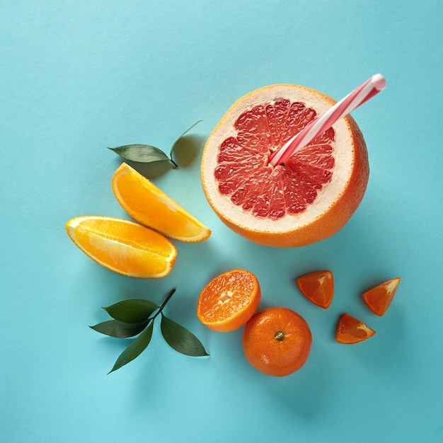 Top view of tropical exotic citrus fruits half a grapefruit, tangerine, and orange slices with a plastic straw