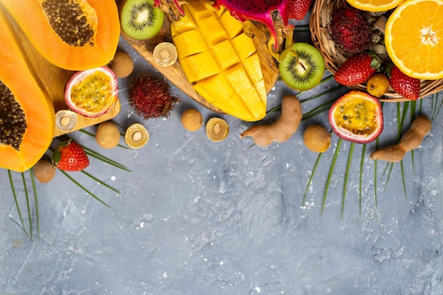 Top view of tropical fruits on grey blue background with free space for your text. Set of dragon fruit, rambutan, tamarind, mango, passion fruit, kiwi, orange, strawberry, leaves. Flat lay.