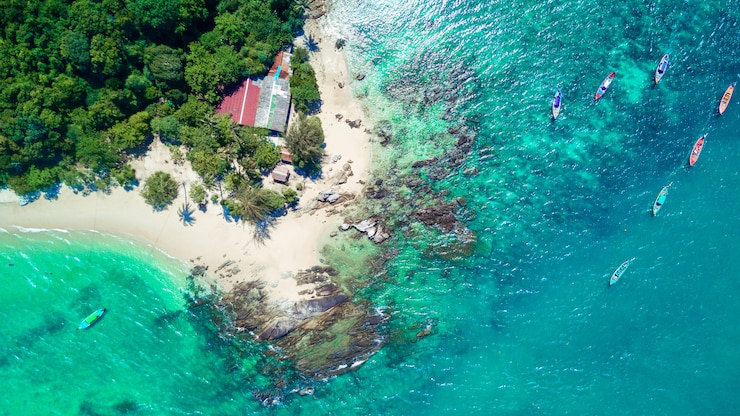 Photo top view: tropical island with palm trees, azure sea and a lot of thai traditional boats next to it.