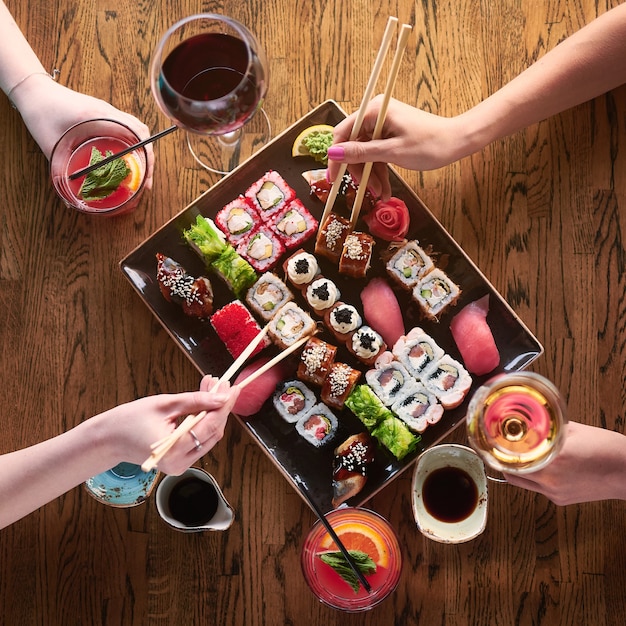 Foto vista dall'alto. due ragazze mangiano sushi. set di vari tipi di panini e sushi con bevande