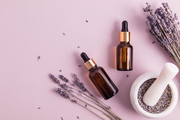 Top view of two glass cosmetic bottles with a pipette with a natural lavender remedy plant twigs a mortar with a pistil and flowers