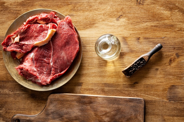 Top view of two pieces of raw meat next to black pepper beans and virgin olive oil. Barbeque preparation.