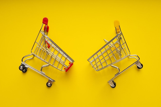 Top view of two supermarket carts for shopping on yellow background Concept of shopping