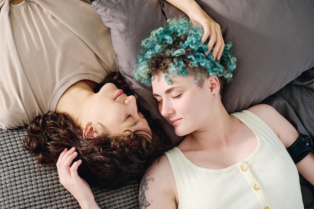 Top view of two young lesbian girlfriends in tshirts lying on bed