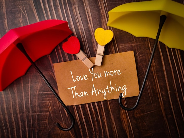 Top view umbrella and brown card with text Love You more than anything on a wooden background