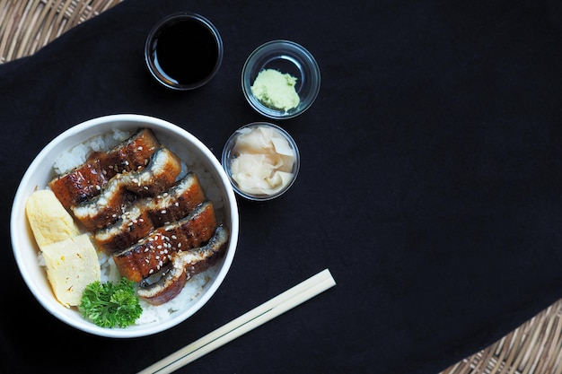 Top view on Unadon or unagi donburi or eel bowl is a dish originating in Japan on black background