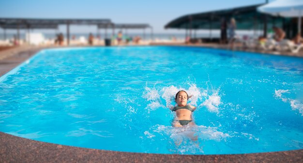 明るい日差しの下でプールの青い澄んだ水に喜んで水しぶきを上げている正体不明のかわいい少女の上面図。ホテルと海でのリラクゼーションのコンセプト。広告スペース