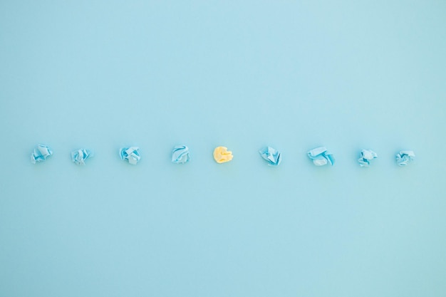 Top view of unique crumpled yellow paper among blue on blue\
background new idea be unique