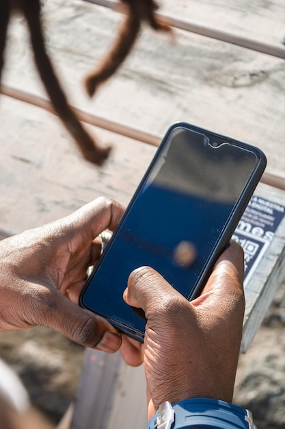 Top view of unrecognizable black man hands using a phone outdoors at sunset image vertical