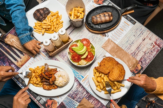 Top view of unrecognizable people eating different types of fried and grilled foods for lunch o dinner