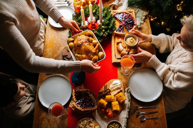 Photo top view of unrecognizable young father putting dish with baked hot turkey on holiday dinner table