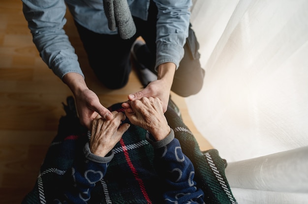 Top view unrecognizable young person holding hands of old woman. Elderly, care, family concept.