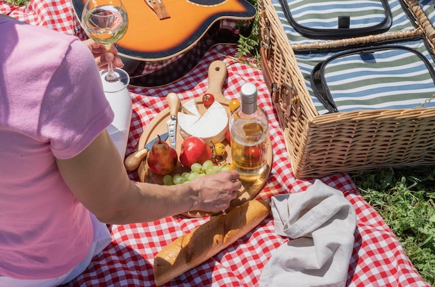 Foto vista dall'alto di una giovane donna irriconoscibile in pantaloni bianchi fuori che fa picnic mangiando e suonando la chitarra vista da dietro