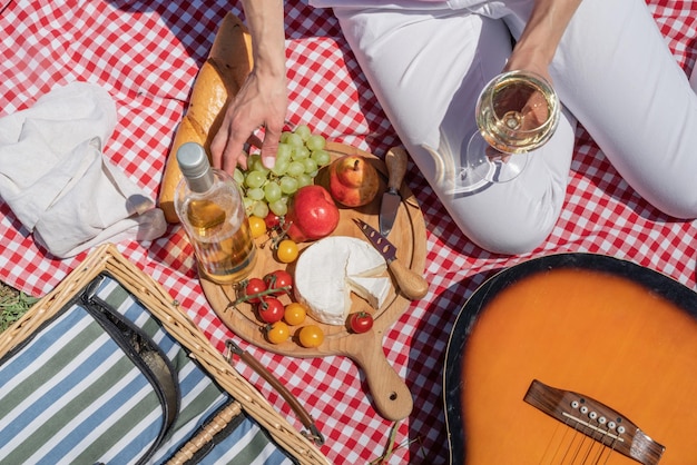 Top view of unrecognizable young woman in white pants outside having picnic eating and playing guitar