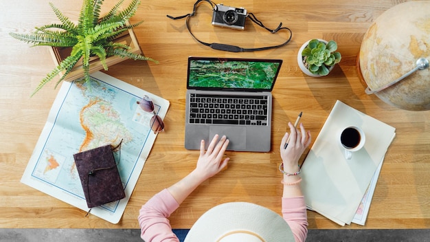 Photo top view of unrecognizable young woman with laptop and maps planning vacation trip holiday