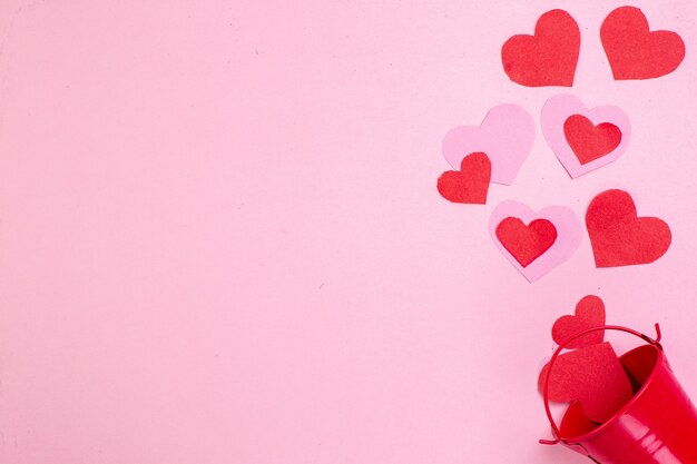 top view valentines day concept red heart stickers scattered from bucket on pink background with free space