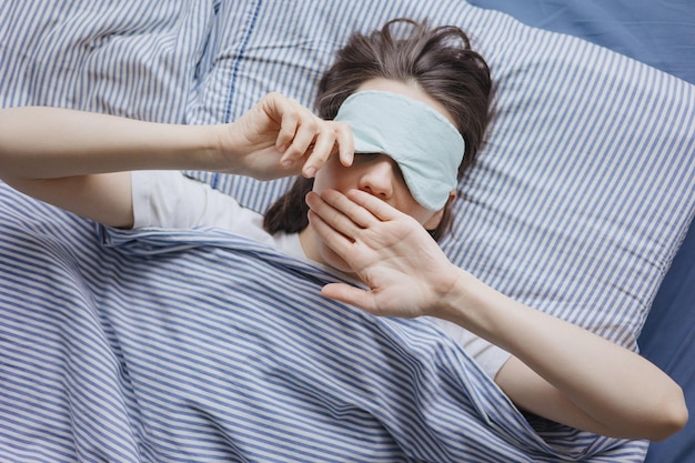 top view van een vrouw in bed met een slaapmasker een gelukkige Europese vrouw wordt wakker en strekt zich uit doet persoon