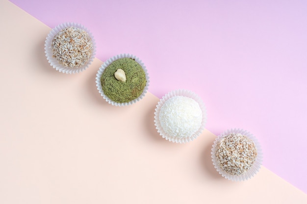 Top view of variety of truffles or energy balls laying in a row on pink and orange background